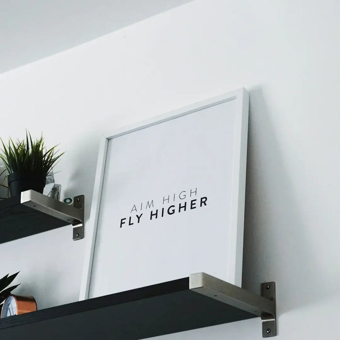 Framed motivational print saying FLY HIGHER on a shelf in modern interior design.