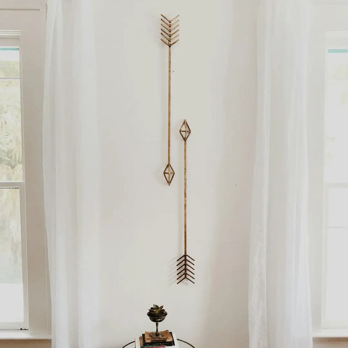 Decorative metal arrow with geometric shapes as modern canvas wall decor on white wall.