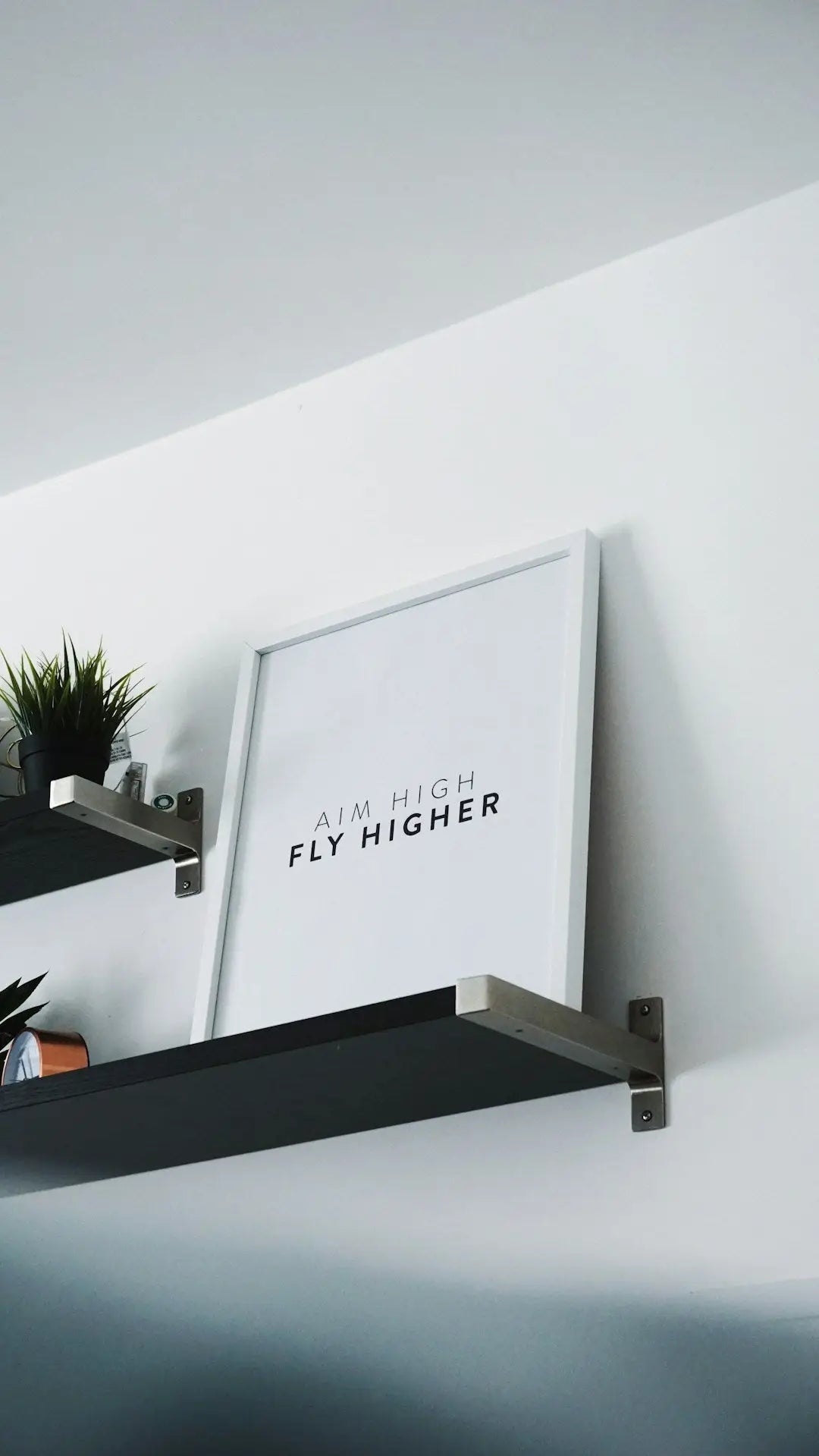 Framed motivational print saying FLY HIGHER on a shelf, enhancing interior design solutions.