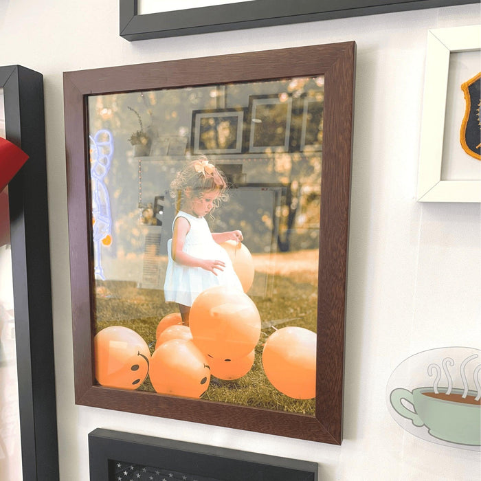 Framed photograph of a young child among orange pumpkins in a brown wood picture frame