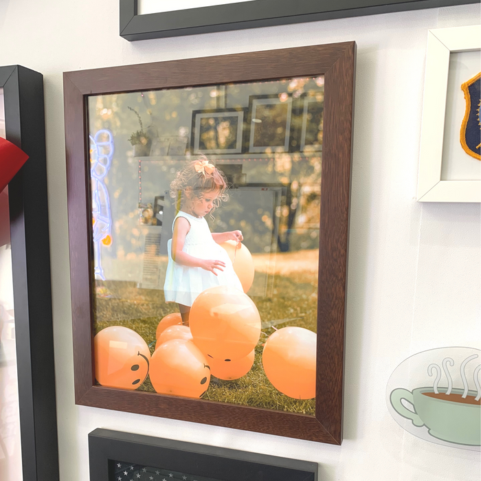 Young child playing with orange balloons in brown wood picture frame wall hanging