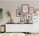 Gallery wall with various artworks in brown wood picture frames above a white cabinet